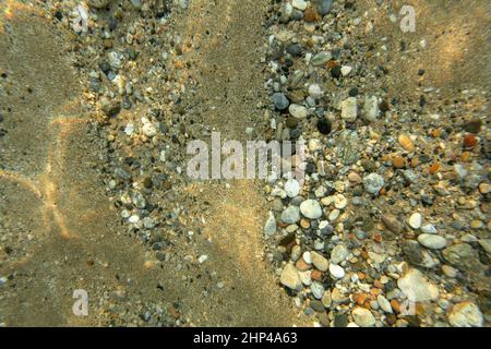 Fotografia subacquea - mare di sabbia sul fondo con piccoli ciottoli e pietre, illuminato dal sole, ripresa dall'alto. Abstract sfondo marino. Foto Stock