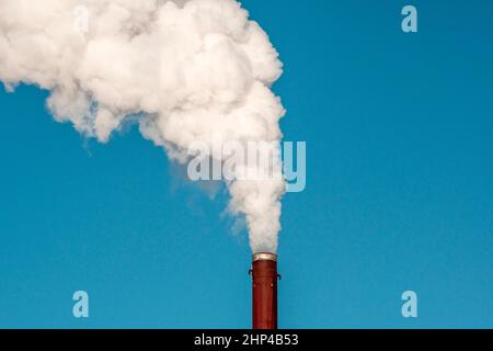 Fumo denso e pesante che esce da un camino arrugginito sotto un cielo blu Foto Stock