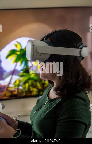 Ragazza con visore VR che gioca con gli amici in realtà virtuale e la proietta sullo schermo tv dietro di lei, Londra, Regno Unito Foto Stock