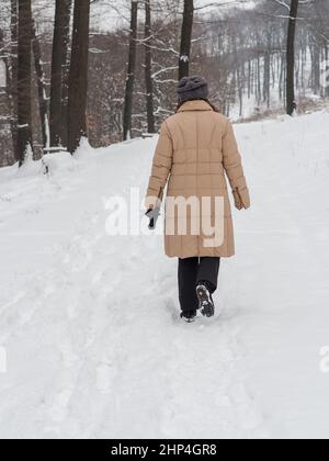 Una donna in un lungo cappotto beige va per una passeggiata nella foresta appena innevata. Foto Stock