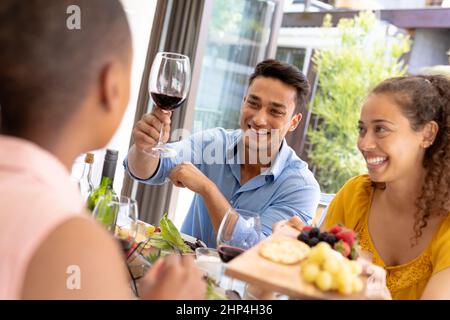 Felice giovane coppia biraciale gustando il pranzo mentre si siede insieme con un amico a tavola Foto Stock