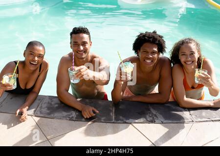 Ritratto di donne di uomini biraciali con bevande godendo giorno di sole a bordo piscina Foto Stock