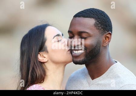 Felice donna caucasica baciare sulla guancia un uomo con la pelle nera Foto Stock