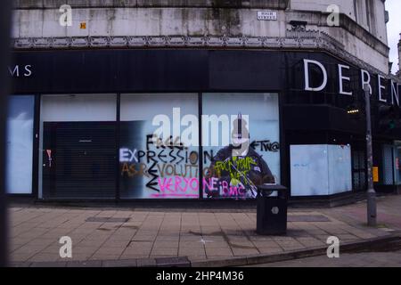 Manchester, Regno Unito, 18th febbraio, 2022. Un umoristico murale che ha visto il primo ministro britannico Boris Johnson nel vecchio negozio Debenhams nel centro di Manchester, Regno Unito, è stato vandalizzato due volte finora con i graffiti. Prodotto da 'Foka Wolf', un artista di strada, il murale ha la testa di Boris Johnson, indossando un cappello da festa, sopra un'immagine di un ufficiale di polizia armato. C'è un'indagine della polizia sui partiti a 10 Downing Street durante i blocchi Covid-19. L'artista ha menzionato ciò che vede come "doppio standard" del governo. Credit: Terry Waller/Alamy Live News Foto Stock