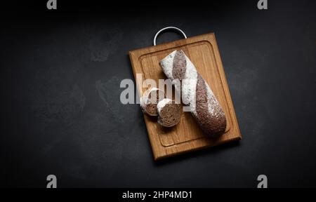 baguette di farina di segale a fette si trova su un asse di legno marrone, vista dall'alto Foto Stock