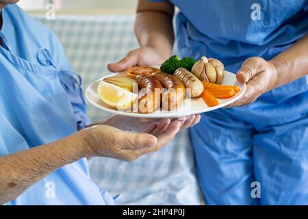 Donna anziana o anziana asiatica donna anziana che mangia la colazione e verdura cibo sano con speranza e felice mentre si siede e affamato a letto in hosp Foto Stock