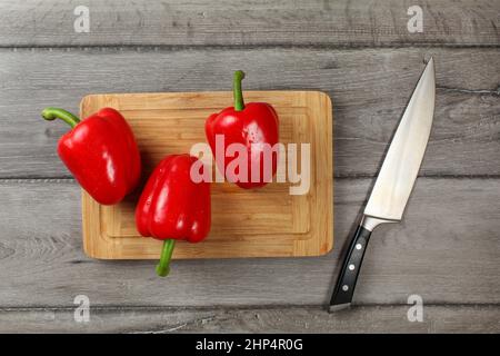 Vista del piano portapaziente - tre interi di peperoni rossi sul tagliere, coltello accanto ad essa, pronta per essere tagliata. Foto Stock