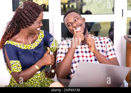 Seri uomini d'affari adulti seduti su sedie e lavorando insieme su un computer portatile mostrando i loro pollici. Foto Stock