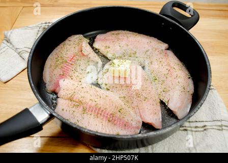 Frittura di Tilapia fresca in una padella nera con burro ed erbe Foto Stock