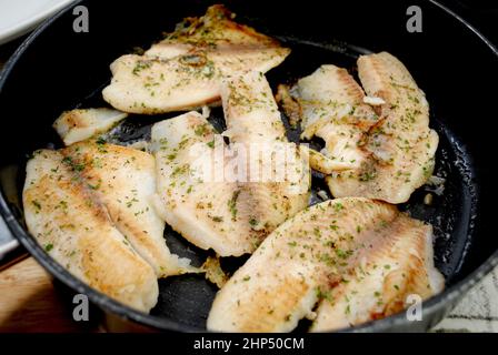 Frittura di Tilapia fresca in una padella nera con burro ed erbe Foto Stock