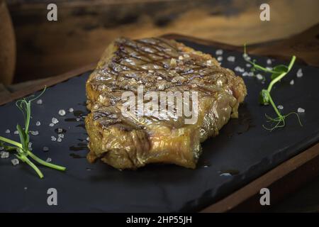 ribeye steak lezhin su un basamento di pietra e legno, decorato con microgreens e grandi cristalli di sale, stile rustico, primo piano, vista laterale Foto Stock