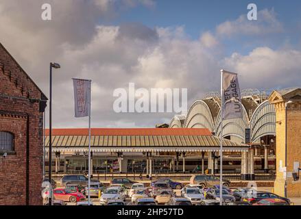 L'architettura storica di una stazione ferroviaria. Quattro grandi archi sono su un lato e un baldacchino 19th secolo copre una piattaforma. Un parcheggio auto è nel fo Foto Stock