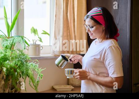 Donna di mezza età a casa in cucina che fa il caffè in un cezve di ferro Foto Stock