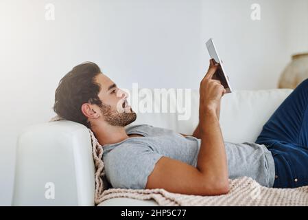 Recuperare i miei programmi settimanali preferiti. Scatto di un giovane che naviga in Internet a casa su un tablet digitale. Foto Stock