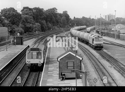 Un'unità multipla diesel di Classe 121 numero L128 che forma un servizio di rete sud-est si ferma alla linea principale di Acton mentre la locomotiva diesel di Classe 60 numero 60056 che lavora un treno di serbatoi di olio di carrello attende un percorso a nord nel cortile di Acton. 10th giugno 1991. Foto Stock