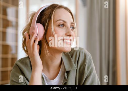 Sorridente giovane donna bianca bionda in cuffie in piedi a casa Foto Stock