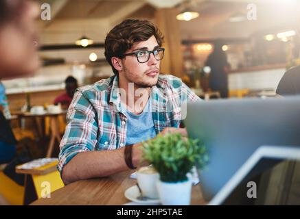 Resta concentrato e non rinunciare mai. Scatto corto di un giovane seduto in un caffè. Foto Stock