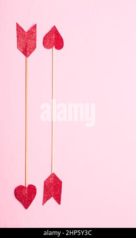 Scatto verticale di due frecce in paillettes rosse a forma di cuore Foto Stock