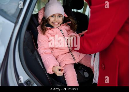 Amorevole madre premurosa fissa la sua bambina nel sedile dell'automobile, allacciando la cintura di sicurezza della bambina adorabile mentre viaggia insieme in auto al Wi meraviglioso Foto Stock