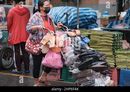 Un venditore itinerante a Pak Klong Talat (mercato) a Bangkok, spingendo il suo carrello carico di scarpe Foto Stock