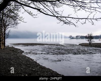 Un piccolo ruscello che scorre nell'acqua di Coniston, con la cima delle montagne sullo sfondo avvolta dalla nebbia Foto Stock