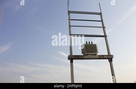 Chiudere il trasformatore su un palo di cemento. Trasformatori trifase e zattere su binari per impianti industriali su sfondo cielo blu. Selettivo foc Foto Stock