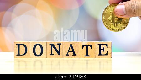 Mani ravvicinate di un uomo che tiene la moneta d'oro per dare a donare lettere di legno su bokeh sfondo sfocato Foto Stock