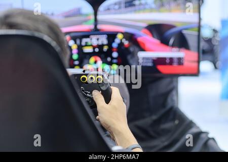 Primo piano dalla vista posteriore mano destra del giovane giocatore che si diverte con il gioco di corse tramite il controller della ruota di gioco sul monitor di gioco, e-sport Foto Stock