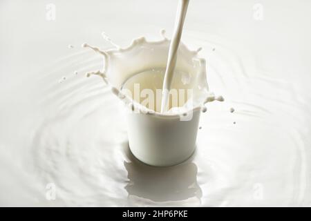 latte versato in vetro con spruzzi su sfondo bianco Foto Stock