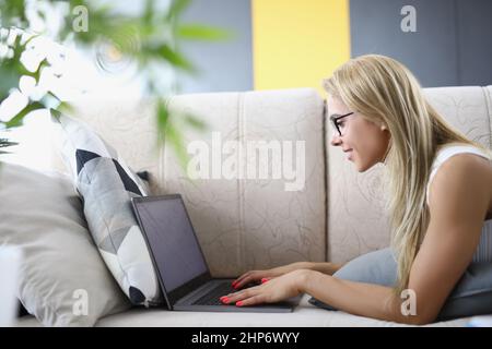 Donna con notebook a casa sdraiata sul divano Foto Stock