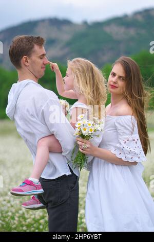 Famiglia felice sul grande prato di montagna camomilla. Scena emozionale, d'amore e di cura. Foto Stock