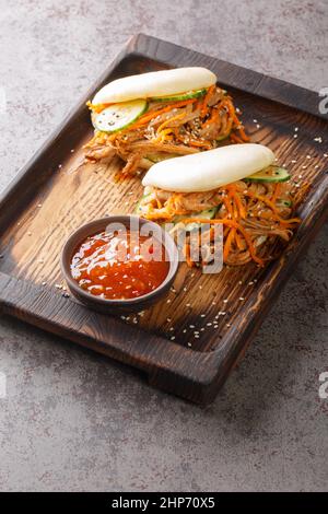 Carne di maiale tirata e verdure al vapore Bao Buns primo piano nel bordo sul tavolo. Verticale Foto Stock