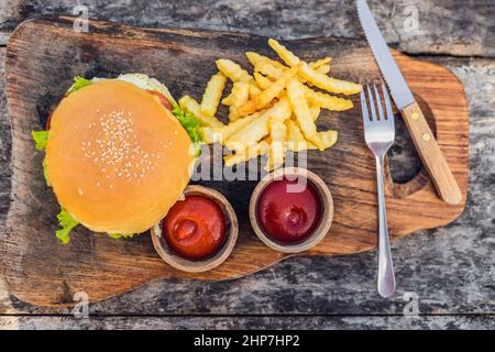 Primo piano di hamburger fresco con patatine fritte su tavola di legno con ciotole di salsa di pomodoro. Cibo lifestyle Foto Stock