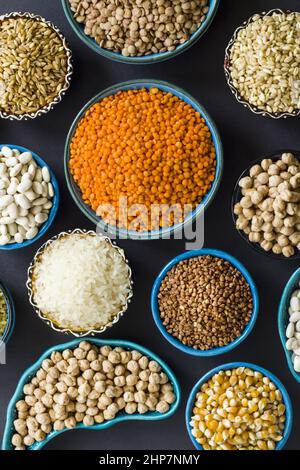 Gruppo di alimenti a base di cereali secchi non cotti in ciotole di ceramica su superficie nera.immagine verticale Foto Stock