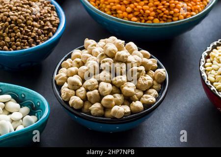 Gruppo di alimenti a base di cereali secchi non cotti in ciotole di ceramica su superficie nera. Ciotola di ceci selezionata Foto Stock