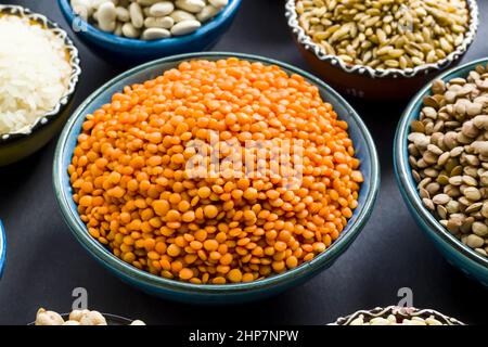 Gruppo di alimenti a base di cereali secchi non cotti in ciotole di ceramica sulla superficie nera. Ciotola di lenticchie rosse selezionata Foto Stock