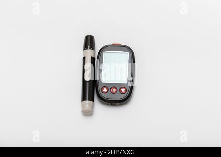 Un piccolo glucometro nero con una penna e una striscia per misurare lo zucchero nel sangue. Il glucometro è isolato su sfondo bianco. Foto Stock