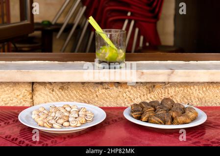 Due piatti con diverse lumache e un bicchiere di caipirinha Foto Stock