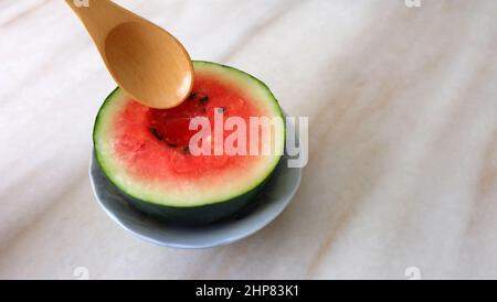 Cucchiaio di legno cercando di scavare in un piccolo cocomero tagliato a metà. Con spazio di copia sulla destra. Foto Stock