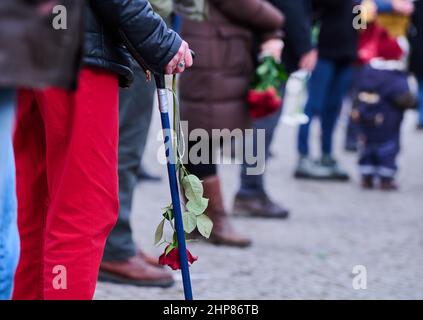 19 febbraio 2022, Berlino: La gente tiene le rose nelle loro mani mentre partecipa alla cerimonia commemorativa che segna l'anniversario degli attacchi di Hanau. La commemorazione in occasione del secondo anniversario degli attacchi razzisti di Hanau è stata organizzata dall'alleanza Treptow-Köpenick ricorda Hanau e si è svolta nella piazza del mercato di Berlino-Adlershof. Foto: Annette Riedl/dpa Foto Stock