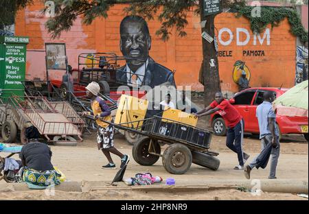 KENYA, Nairobi, Slum Kibera, elezione presidenziale 2022, affissioni del candidato Raila Amollo Odinga del partito ODM Orange Democratic Movement, facchino trasporto di scatole con birra Tusker di birrifici dell'africa orientale Ltd. Di proprietà di Diageo Group UK / KENIA, Nairobi, Slum Kibera, Präsidenten Wahl 2022, Wandbild des Kandidaten Raila Amollo Odinga von der ODM Orange Democratic Movement Partei, Lastkarren mit Bierkisten mit Tusker Bier der Ostafrikanischen Brauerei der Diageo Group, Inghilterra Foto Stock