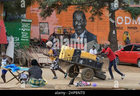 KENYA, Nairobi, Slum Kibera, elezione presidenziale 2022, affissioni del candidato Raila Amollo Odinga del partito ODM Orange Democratic Movement, facchino trasporto di scatole con birra Tusker di birrifici dell'africa orientale Ltd. Di proprietà di Diageo Group UK / KENIA, Nairobi, Slum Kibera, Präsidenten Wahl 2022, Wandbild des Kandidaten Raila Amollo Odinga von der ODM Orange Democratic Movement Partei, Lastkarren mit Bierkisten mit Tusker Bier der Ostafrikanischen Brauerei der Diageo Group, Inghilterra Foto Stock