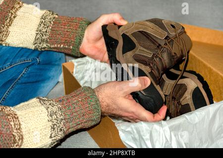 L'uomo tiene uno stivale in mano. Le mani maschili mostrano una scarpa alta. Un uomo tira una scarpa fuori del box.close-up.concept di acquisto, cercando di scarpe e stivali. Foto Stock