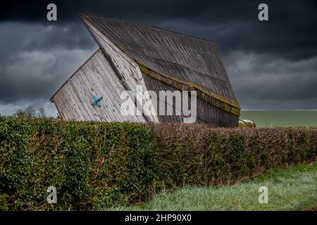 un edificio di scuderie di cavalli di legno soffiato su un lato durante i venti estremi forti, tuono tempesta cielo nuvoloso scuro Foto Stock