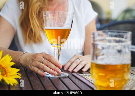 Donna seduta in ristorante all'aperto e bere birra, vita cittadina in estate. Donna che tiene un bicchiere di birra alla spina nel pub Foto Stock