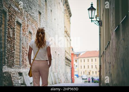 La donna alla moda sta camminando in strada nella città vecchia europea, concetto di moda di donna alla moda. Donna alla moda che indossa pantaloni beige Foto Stock
