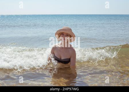 Bella donna in cappello e bikini in acqua di mare sorridente. Passatempo estivo e relax. Foto Stock