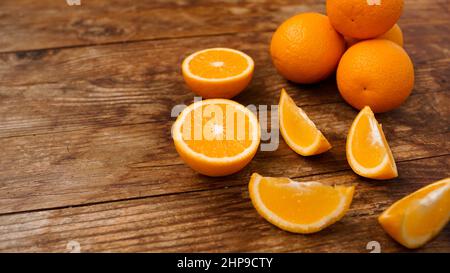 Molte deliziose arance mature su tavola di legno. Frutta a fette e intera per preparare succhi di frutta appena spremuti a colazione. Frutta dolce e succosa Foto Stock