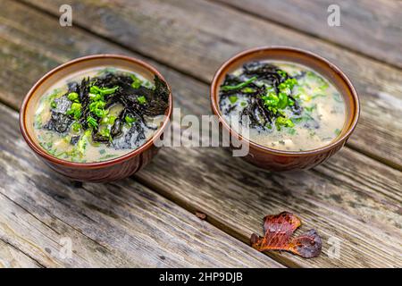 Due ciotole di minestra di miso da vicino con alghe nori e cipolla verde tritata come pasto asiatico giapponese con tavolo di legno e foglia d'autunno Foto Stock