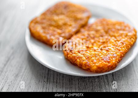 Macro primo piano della colazione o brunch patate fritte due crocchette di patate croccanti hash su piatto bianco con sfondo tavolo in legno Foto Stock